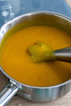 a metal pot filled with yellow soup and a green ladle in front of it