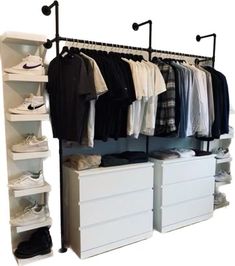 an organized closet with white drawers and black clothes hanging on the rail, along with shoes