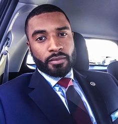 a black and white photo of a man wearing a suit in the back seat of a car