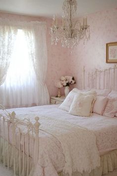 a white bed sitting under a chandelier in a bedroom next to a window