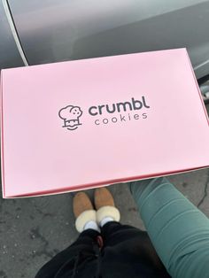 a person holding up a pink box with the word crumbl cookies on it