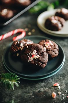 three chocolate cookies on a black plate with candy canes and peppermints in the background