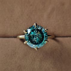 a blue diamond ring sitting on top of a brown velvet covered surface with gold accents