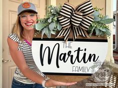 a woman holding up a sign that says the martin family with greenery on it