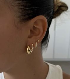 a close up of a person wearing earrings and a white tank top in the background