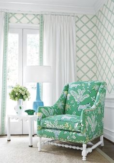 a green chair sitting in front of a window next to a table with a vase on it