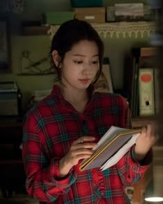 a woman standing in front of a desk holding an open book and looking at it