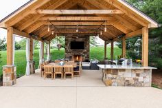 an outdoor kitchen and dining area with wood beams, stone fireplace and grilling station