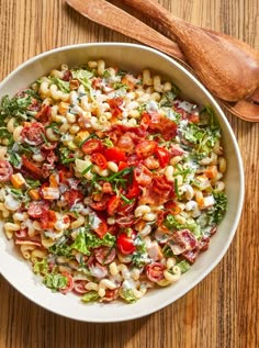 a white bowl filled with pasta salad next to a wooden spoon on top of a table