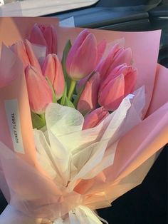 a bouquet of pink tulips wrapped in white paper on the dashboard of a car