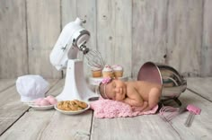 a baby laying on top of a pink blanket next to a mixer and some cookies