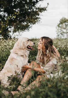 a woman is sitting in the grass with her dog and smiling at each other while they both have their heads close to one another