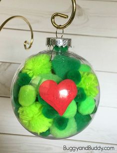 a glass ornament filled with pom - poms and a red heart