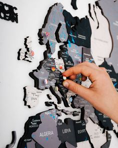 a person's hand pointing at the map of europe on a white wall with black and grey cutouts