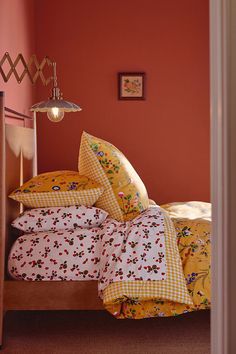 a bed with yellow and red comforters in a bedroom next to an orange wall