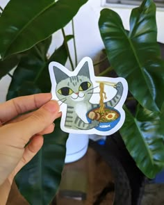 a person holding up a sticker with a cat on it's face and some plants in the background