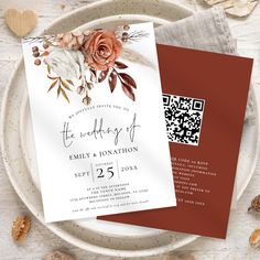 two wedding cards on top of a plate with flowers and leaves in the middle, next to a qr code