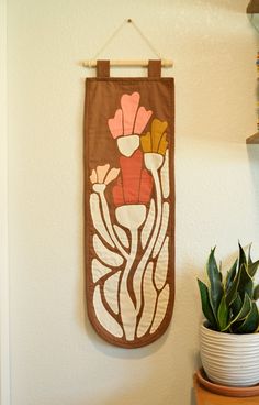 a potted plant sitting on top of a wooden shelf next to a wall hanging