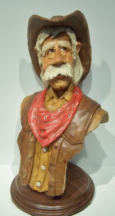 a statue of an old man wearing a cowboy hat and red bandanna on top of a wooden base