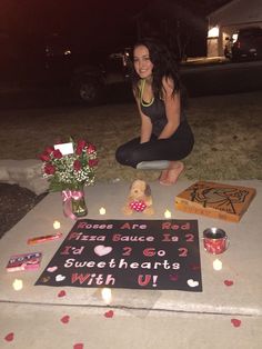 a woman sitting on the ground next to a sign with candles in front of her