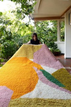 a woman sitting on top of a multicolored rug in front of a house