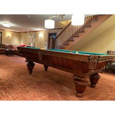 a pool table in the middle of a living room with stairs leading up to it