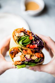 a hand holding a wrap filled with meat and veggies