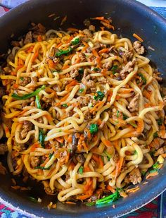 a bowl filled with noodles and meat on top of a blue table cloth next to a fork