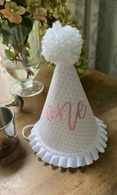 a party hat with the word one on it sitting on a table next to flowers