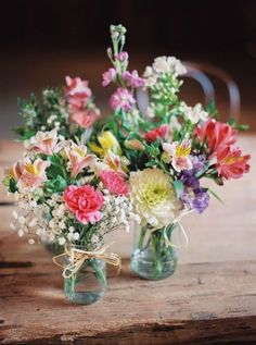 two vases filled with colorful flowers sitting on top of a wooden table next to each other