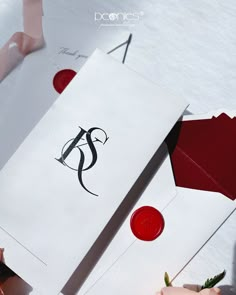 two white envelopes with red and black ink on them, one has a monogram