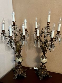 two ornate candelabras with candles on top of them, sitting on a table in front of a wall