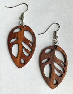 two wooden earrings with leaves cut out of them on a white surface, one is hanging from the earwires