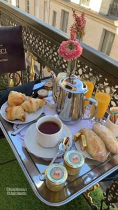 an outdoor table with food and drinks on it, including croissants, muffins, coffee