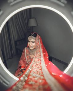 a woman wearing a red and white bridal outfit in front of a round mirror