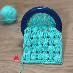 a close up of a knitted object on a wooden surface with yarn in the background