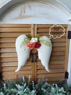 a pair of angel wings hanging from the side of a wooden door next to flowers