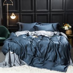 a bed with blue sheets and pillows in a room next to a green chair on the floor