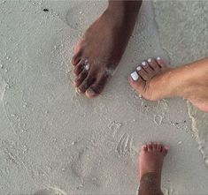 two people standing on the beach with their feet in the sand and one person's bare foot sticking out