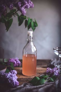 a bottle filled with liquid sitting on top of a wooden table next to purple flowers