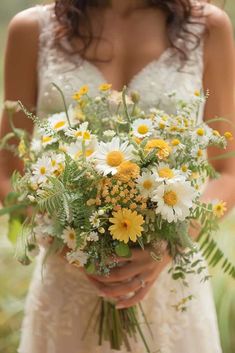 a woman in a wedding dress holding a bouquet of daisies and other wildflowers