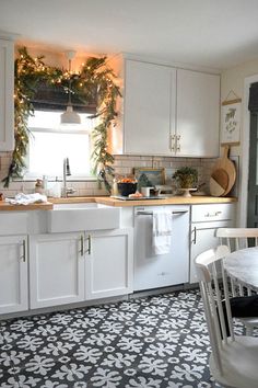 a kitchen with white cabinets and black and white tile flooring that has christmas decorations on the window sill