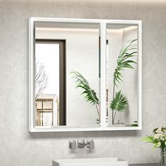 a white sink sitting under a bathroom mirror next to a green plant in a vase