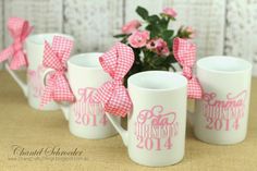 three coffee mugs with bows on them sitting next to a potted plant and pink flowers