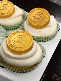 four cupcakes with white frosting and gold foil on top are sitting in a box