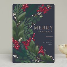 a christmas card with holly and berries on it, next to a gold bowl filled with red berries