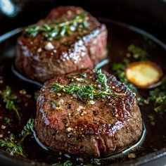 two steaks in a skillet with herbs on top