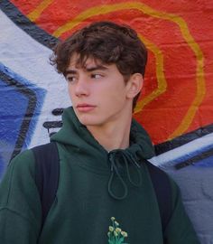 a young man wearing a green hoodie standing in front of a graffiti covered wall