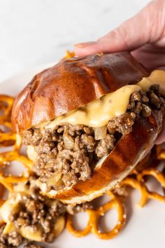 a sandwich with cheese and meat is being held by someone's hand over some cheesy pretzels