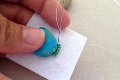 someone is stitching something on top of a piece of white paper with a blue bead